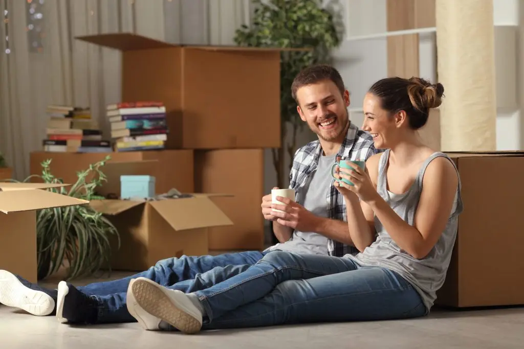 Two young homeowners sitting in their new home, surrounded by boxes