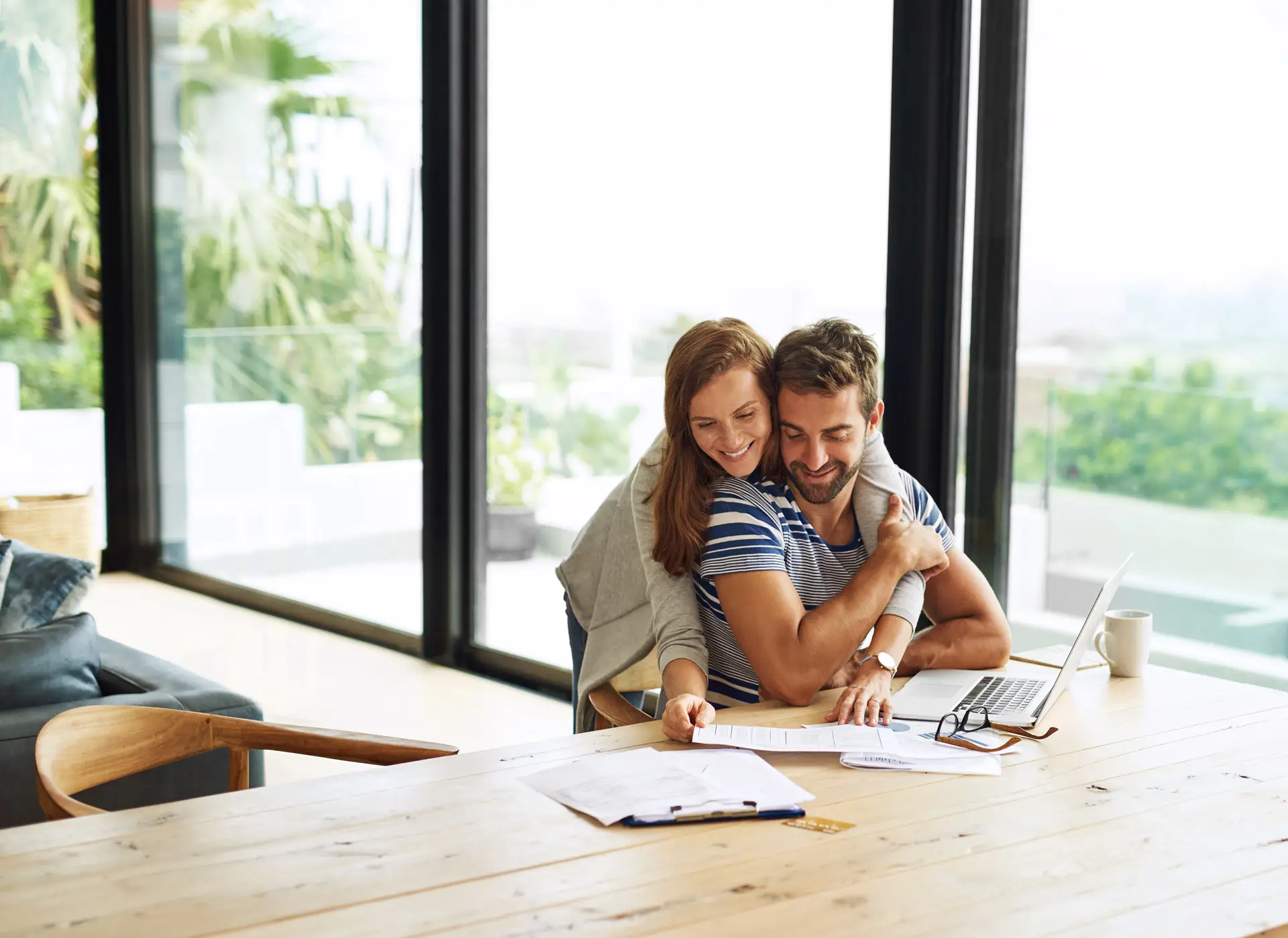 Couple embracing while reviewing financial documents for their new home