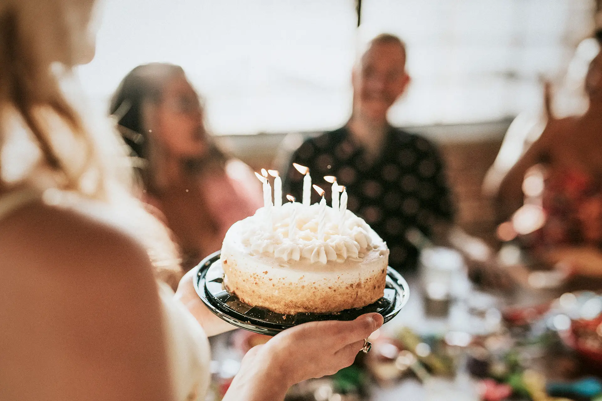 Closeup of someone carrying a birthday cake to a table full of people