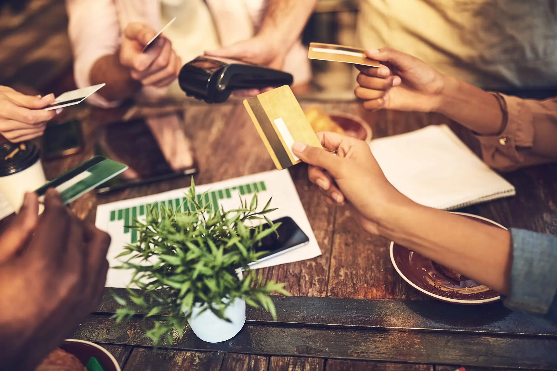 Multiple hands holding out credit cards near a payment terminal