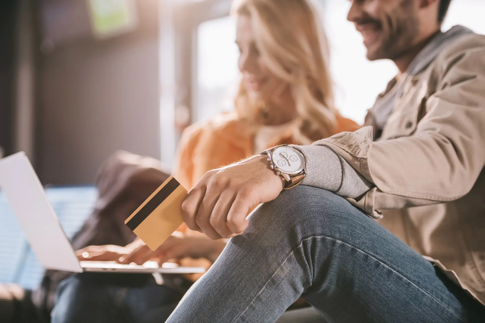 A man holding a credit card while a woman seated beside him uses a laptop