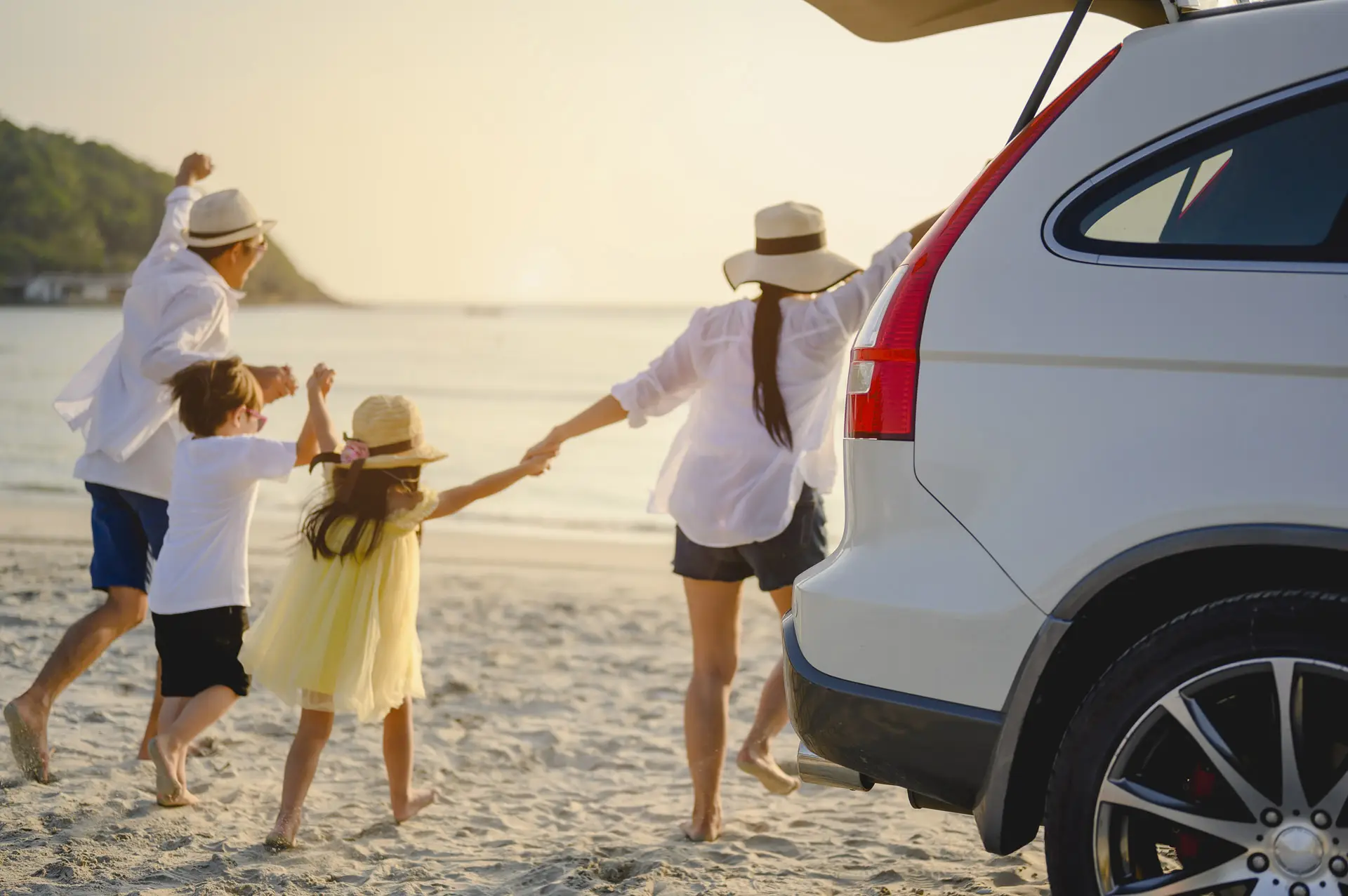 Family running hand in hand on the beach from their car towards the ocean