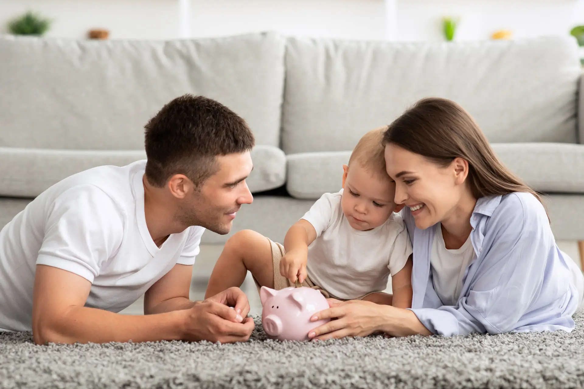 Parents holding a piggy bank while their baby puts a coin in it