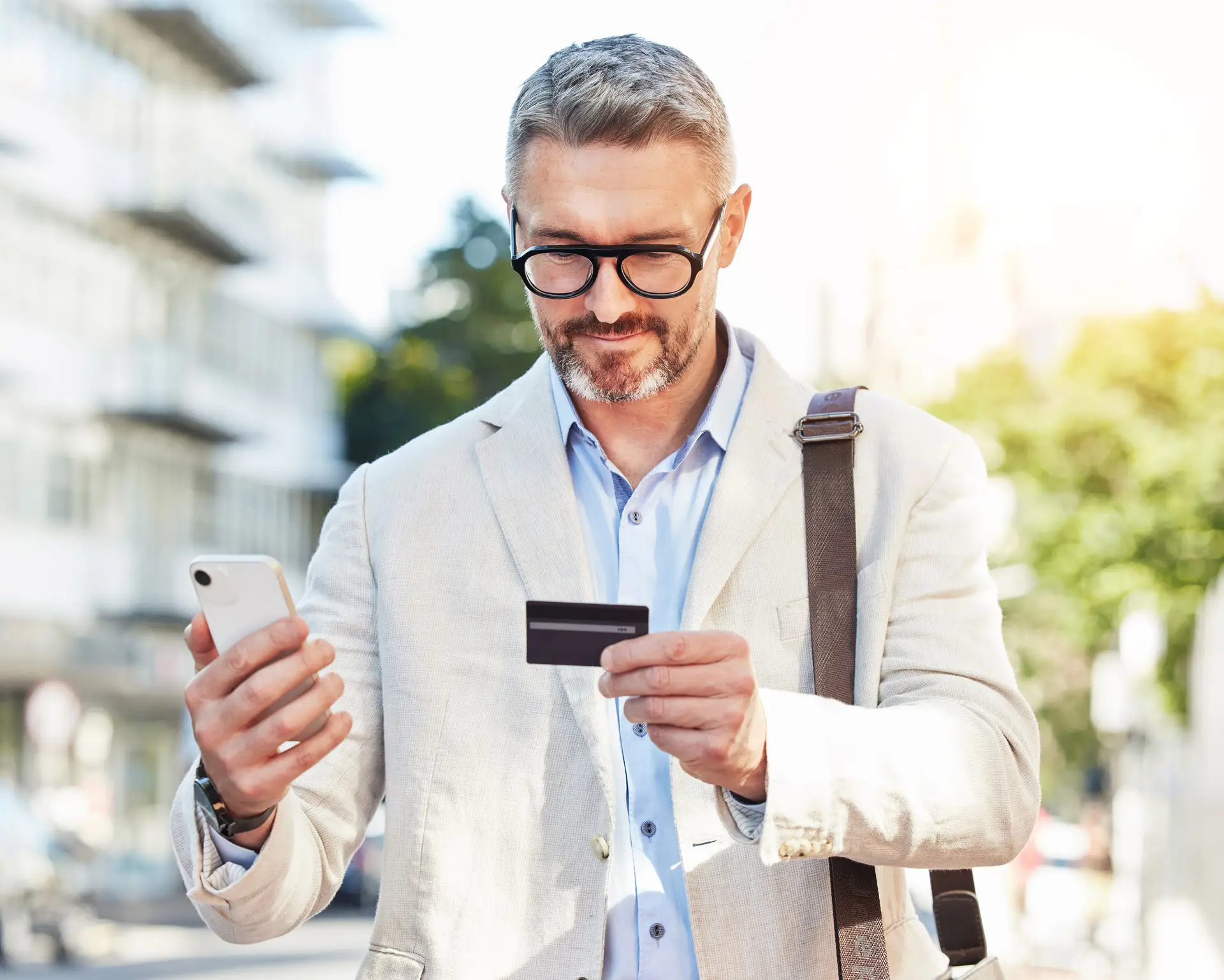 Man outside holding his phone in one hand and a debit card in another