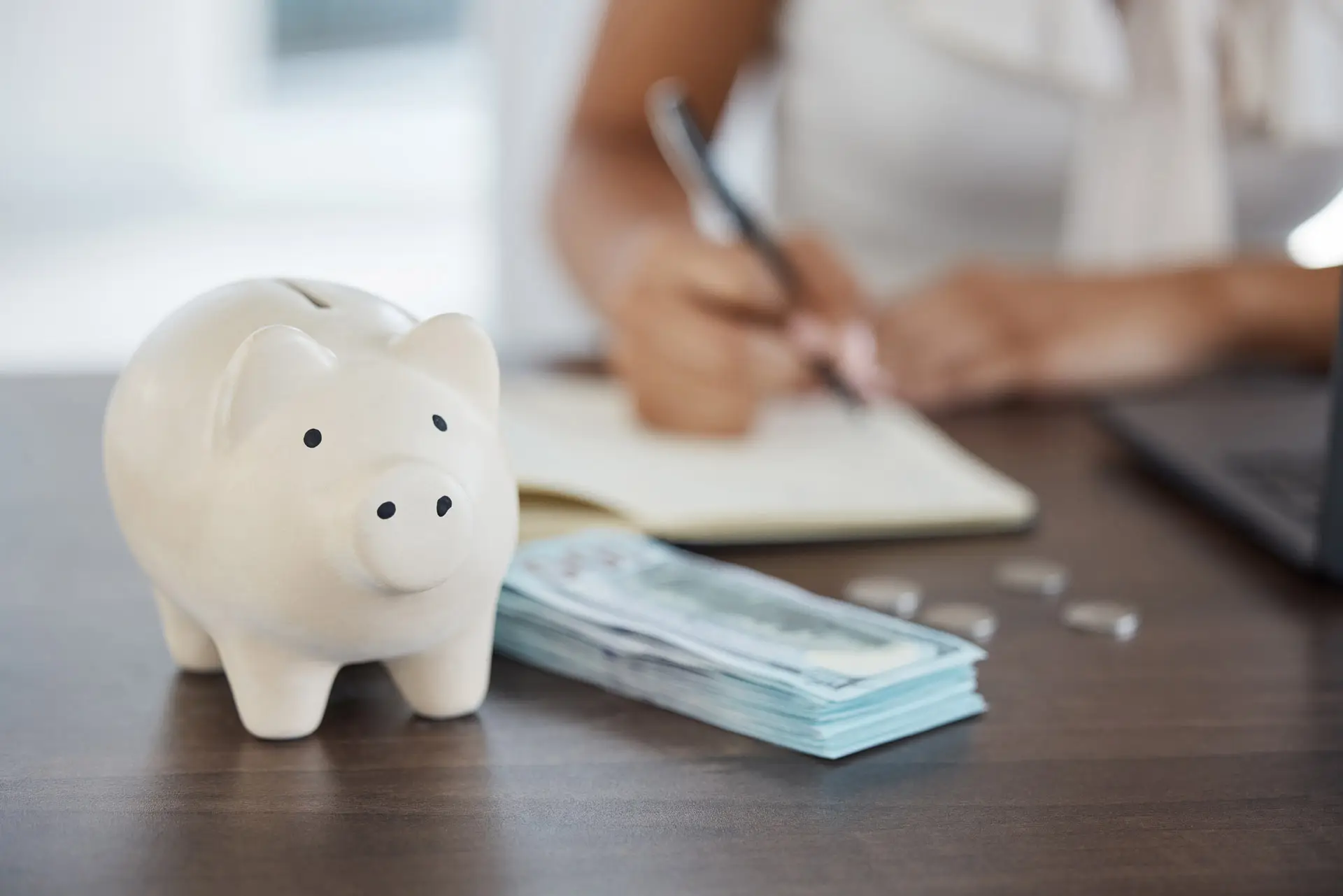 Person writing in a notebook while looking at money and a piggy bank