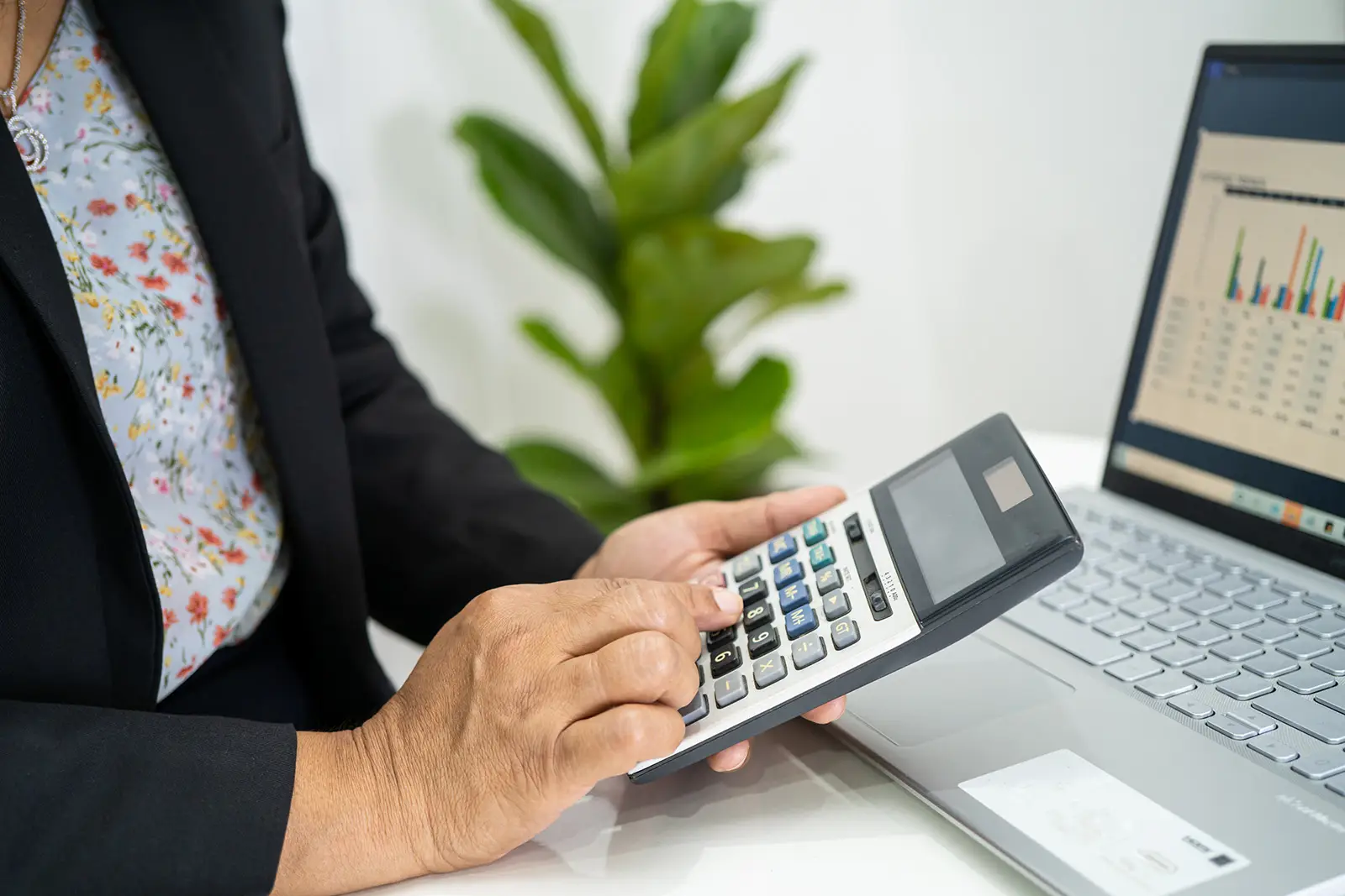 Woman typing on a calculator while looking at a laptop