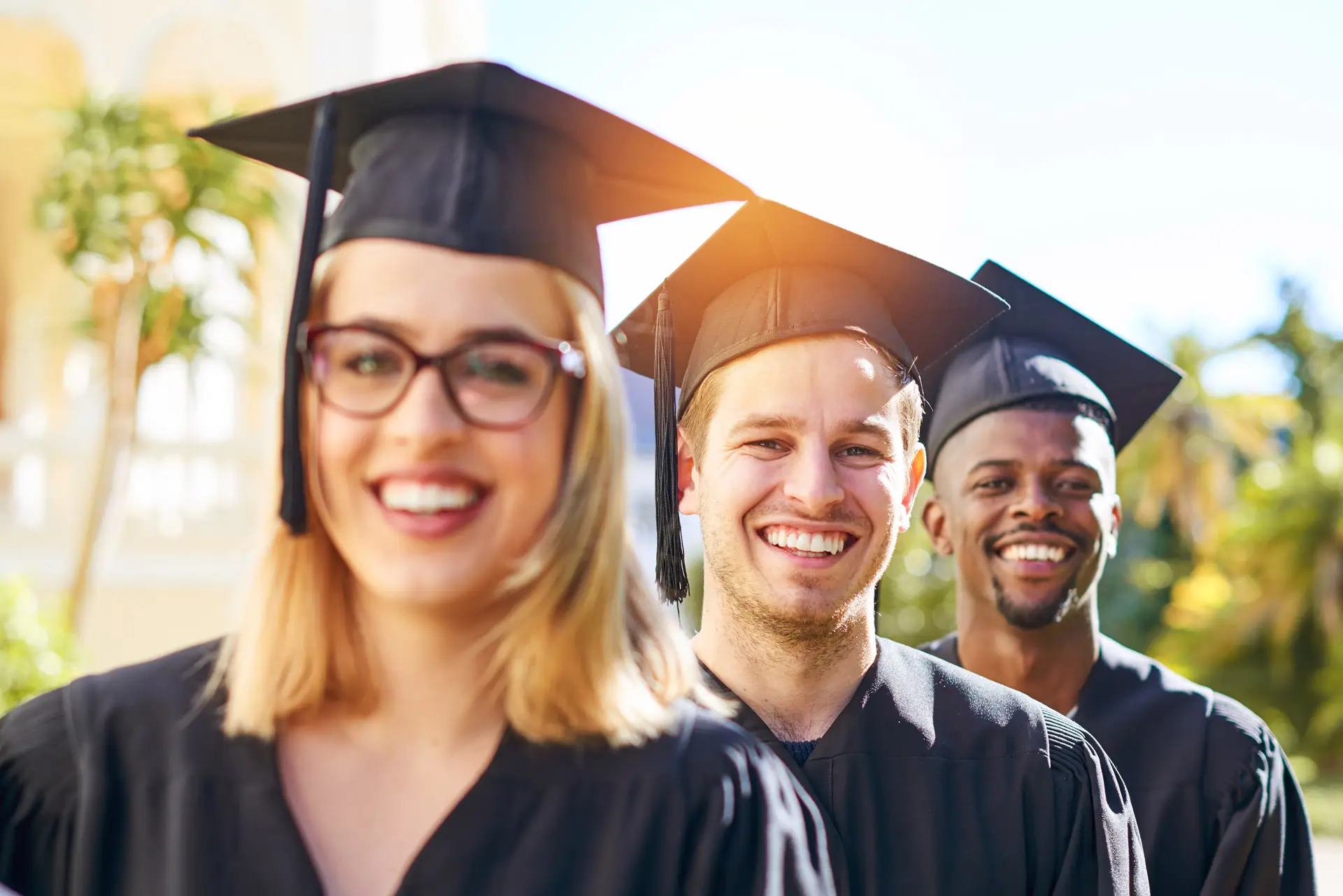 Three graduates in their caps and gowns smiling at the camera