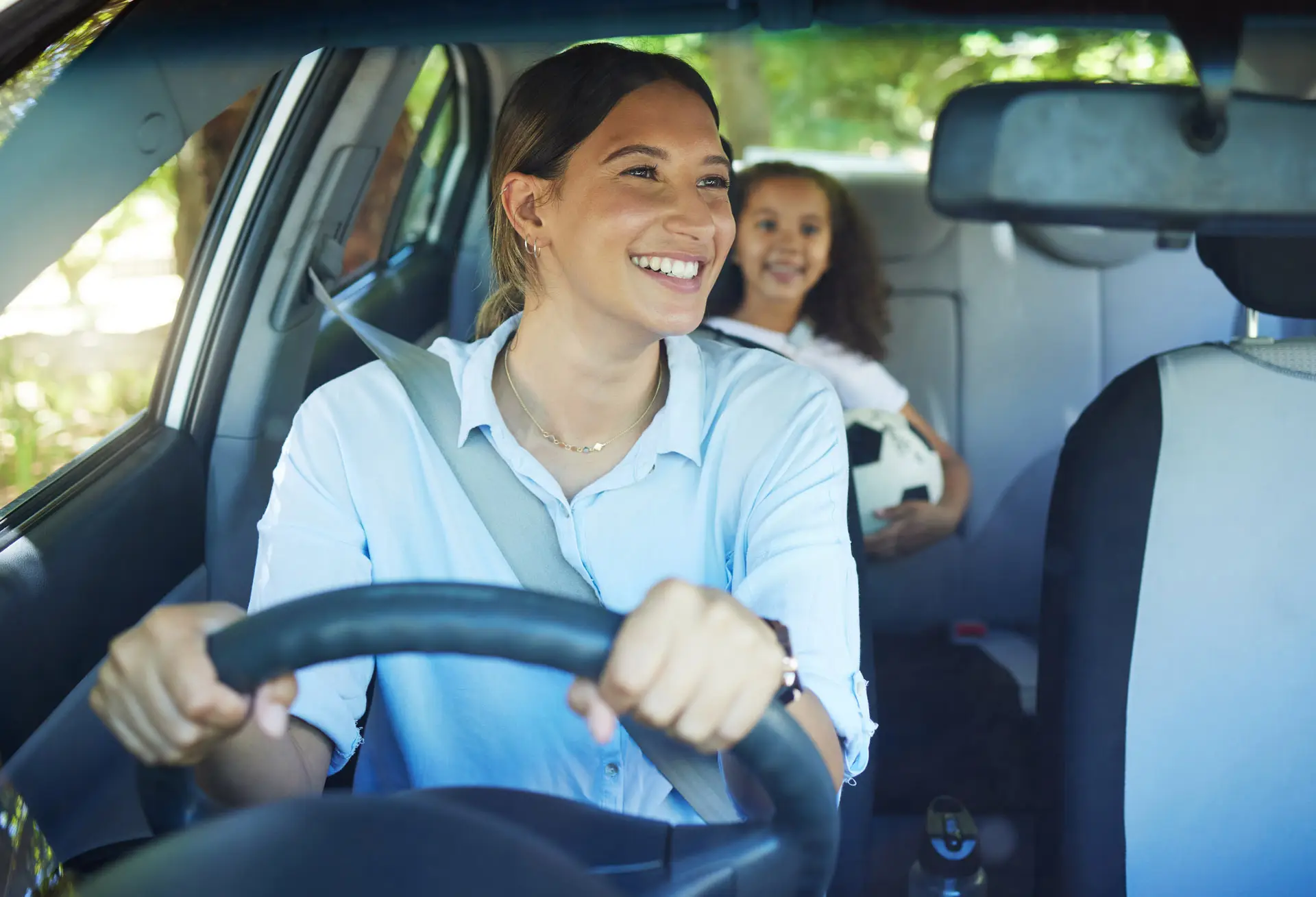 Woman driving a car smiling at her daughter in the back seat